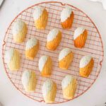 Lavender white chocolate madeleines on a circular rose gold cooling rack.