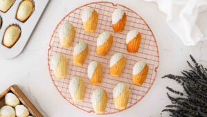 Lavender white chocolate madeleines on a circular rose gold cooling rack.