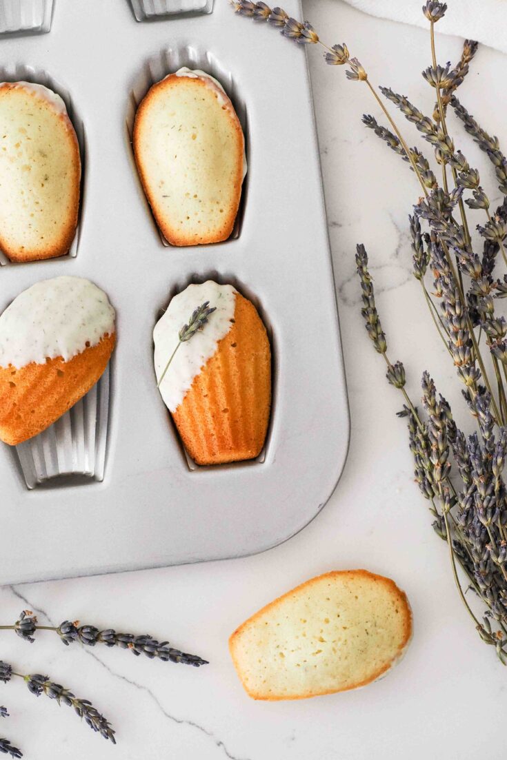 White chocolate-dipped lavender madeleines in the pan with lavender flowers.