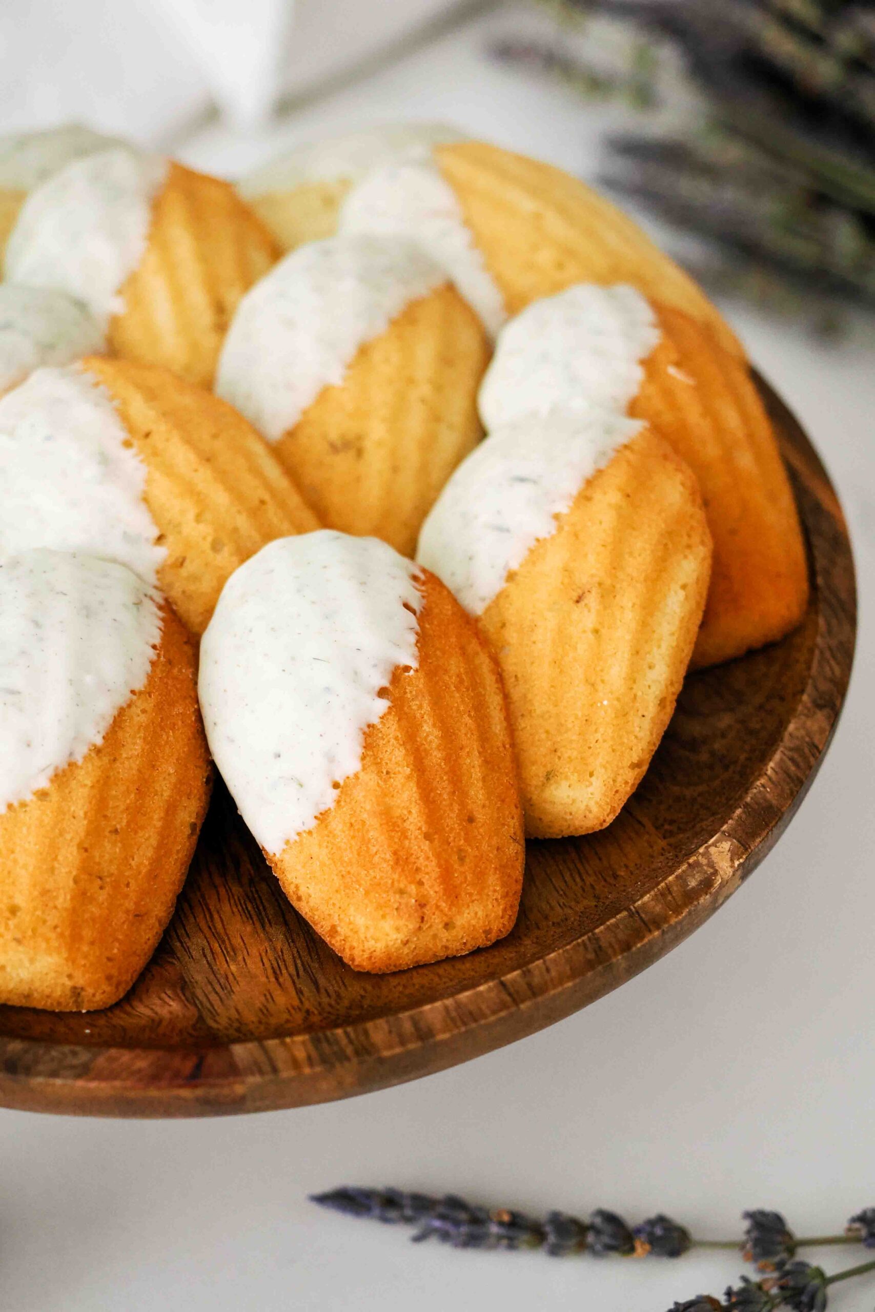 Lavender madeleines dipped in lavender white chocolate on a cake stand.