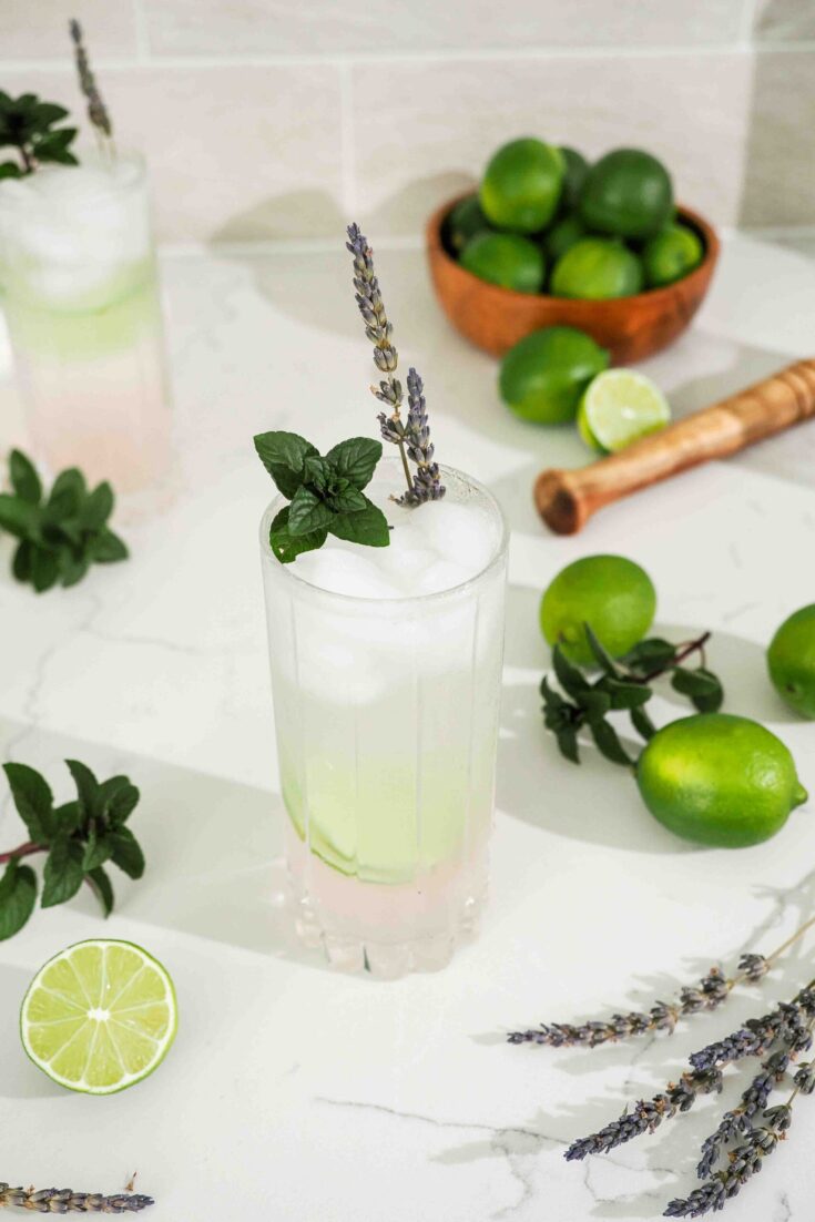 A pink lavender mojito on a quartz counter with limes, mint, and lavender.