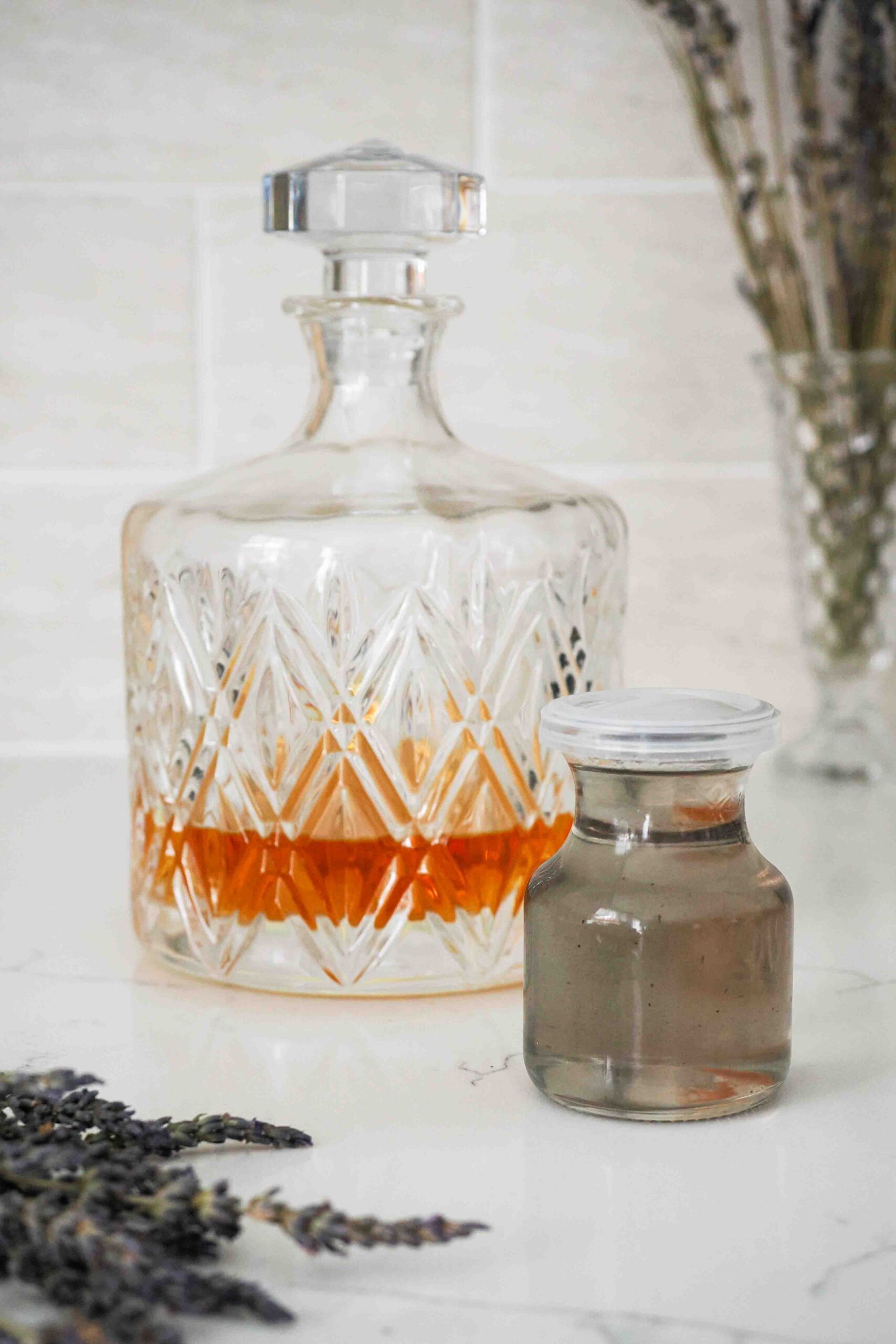 A decanter of whiskey and a bottle of lavender syrup on a counter.