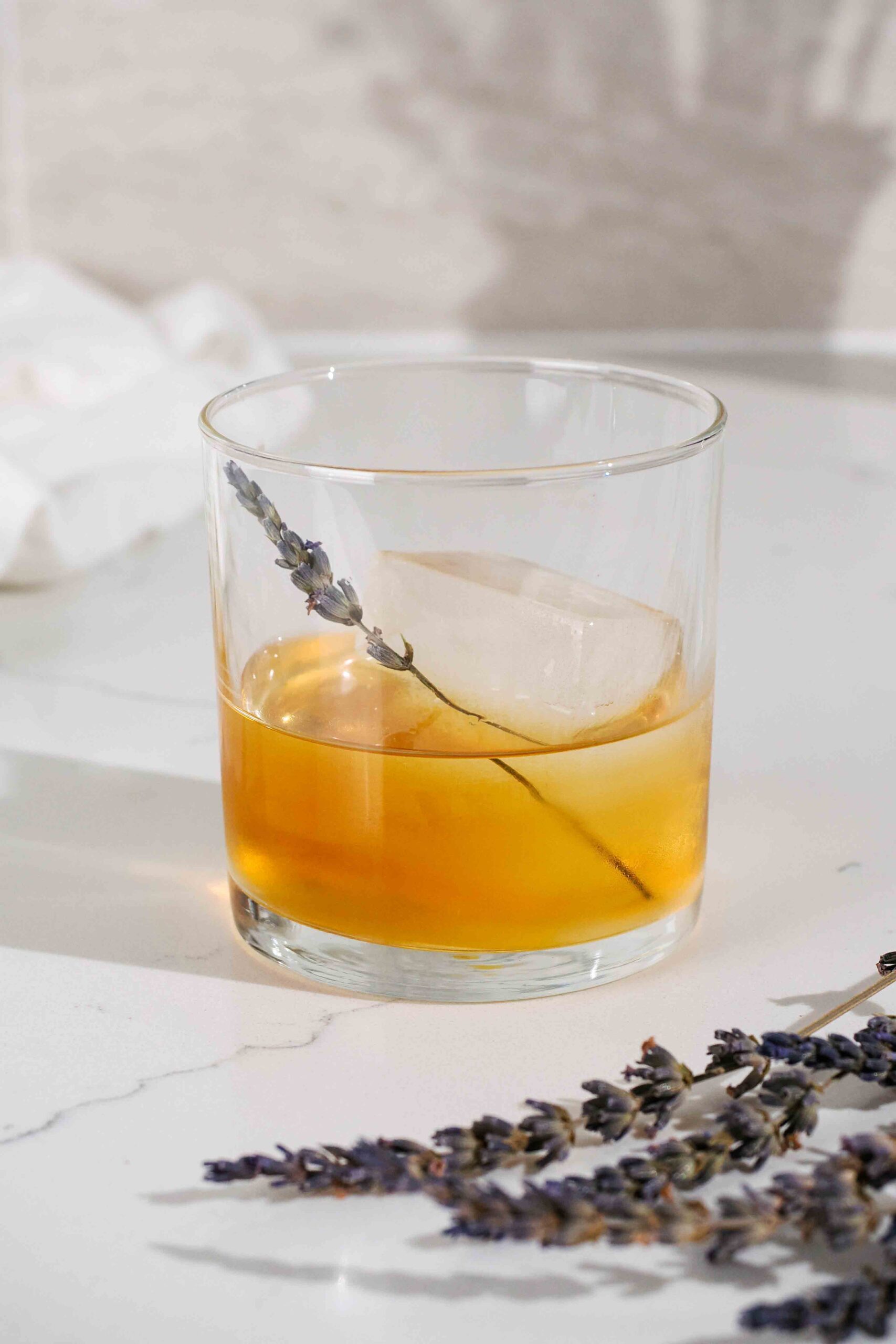 A single rocks glass with a lavender old fashioned on a counter.
