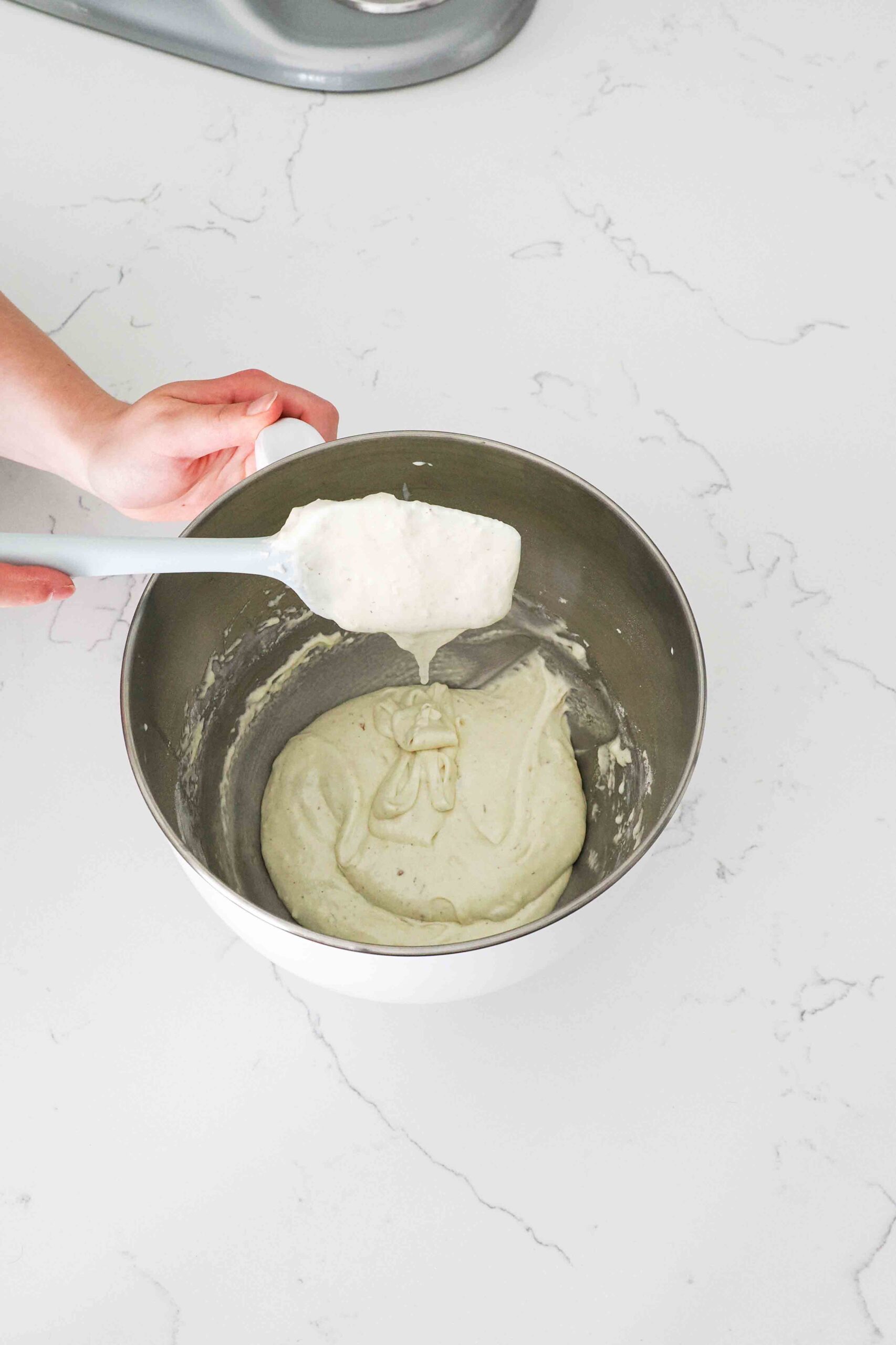 An airy batter falls off the spatula back into a stand mixer bowl.