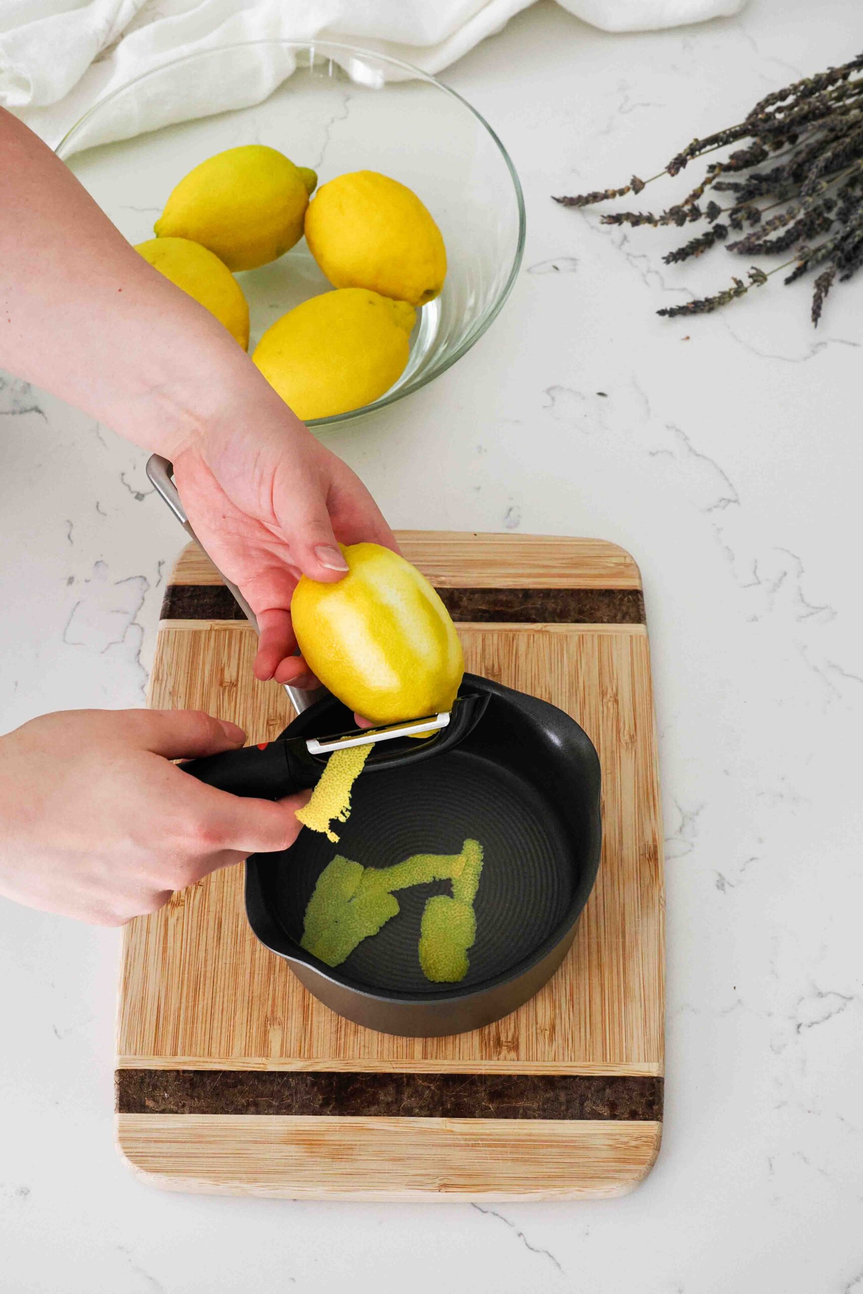 Two hands zest a whole lemon over a small pot.