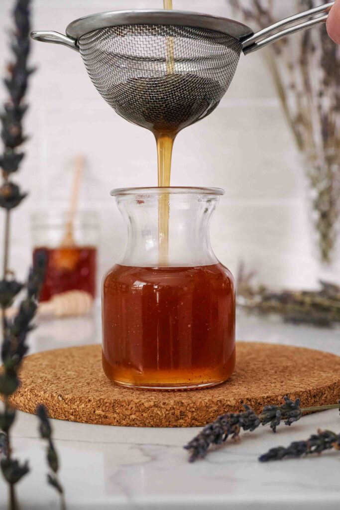 Syrup is poured through a strainer into a small glass bottle.