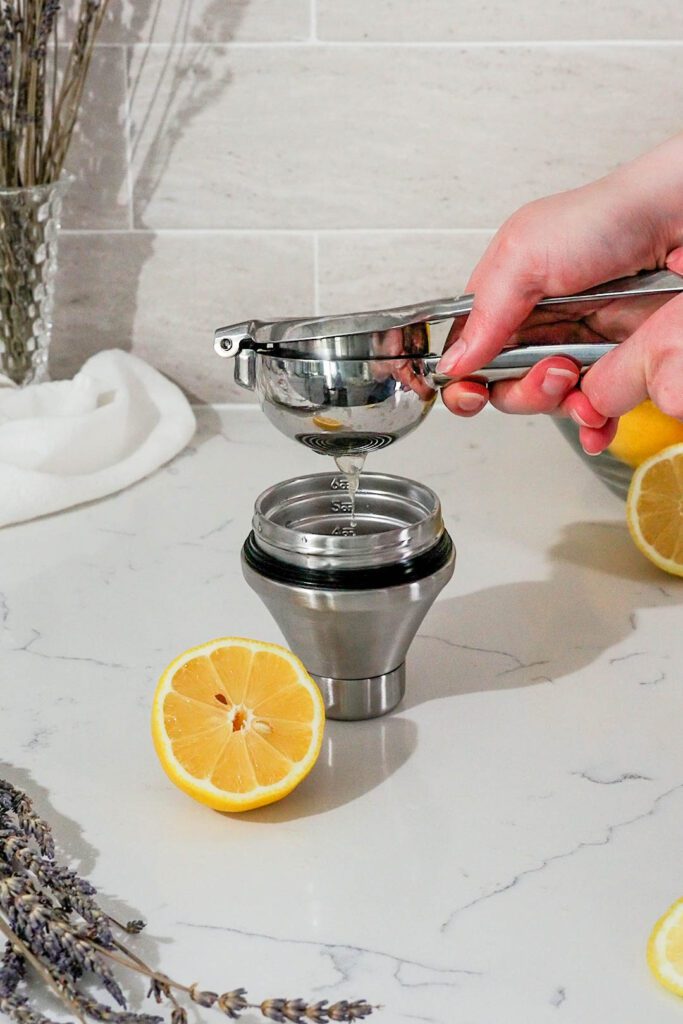 A lemon is squeezed over a jigger with a lemon squeezer.