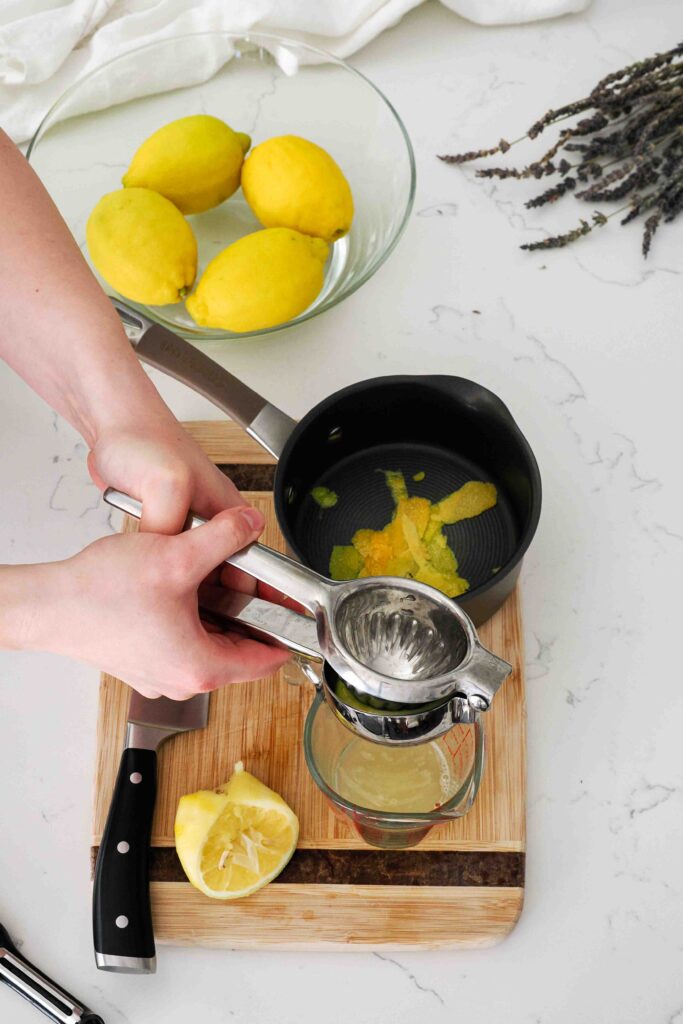 Two hands squeeze a lemon's juice into a measuring cup.