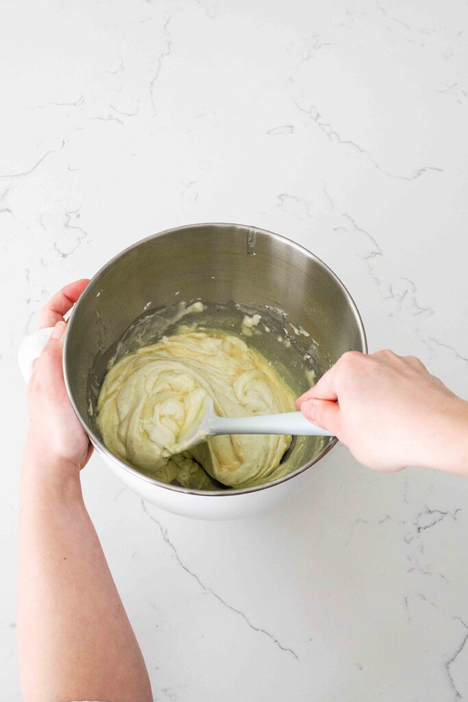 A spatula begins to fold butter into the lavender madeleine batter in a stand mixer bowl.