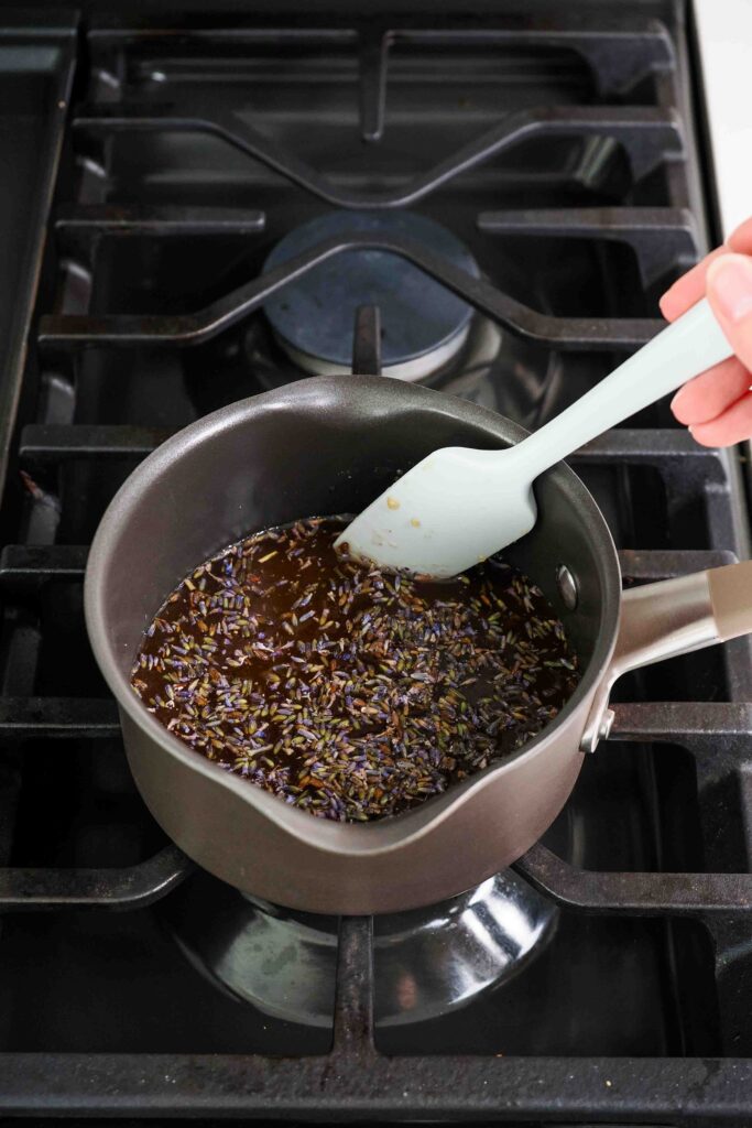 A spatula stirs honey lavender syrup in a small saucepan.