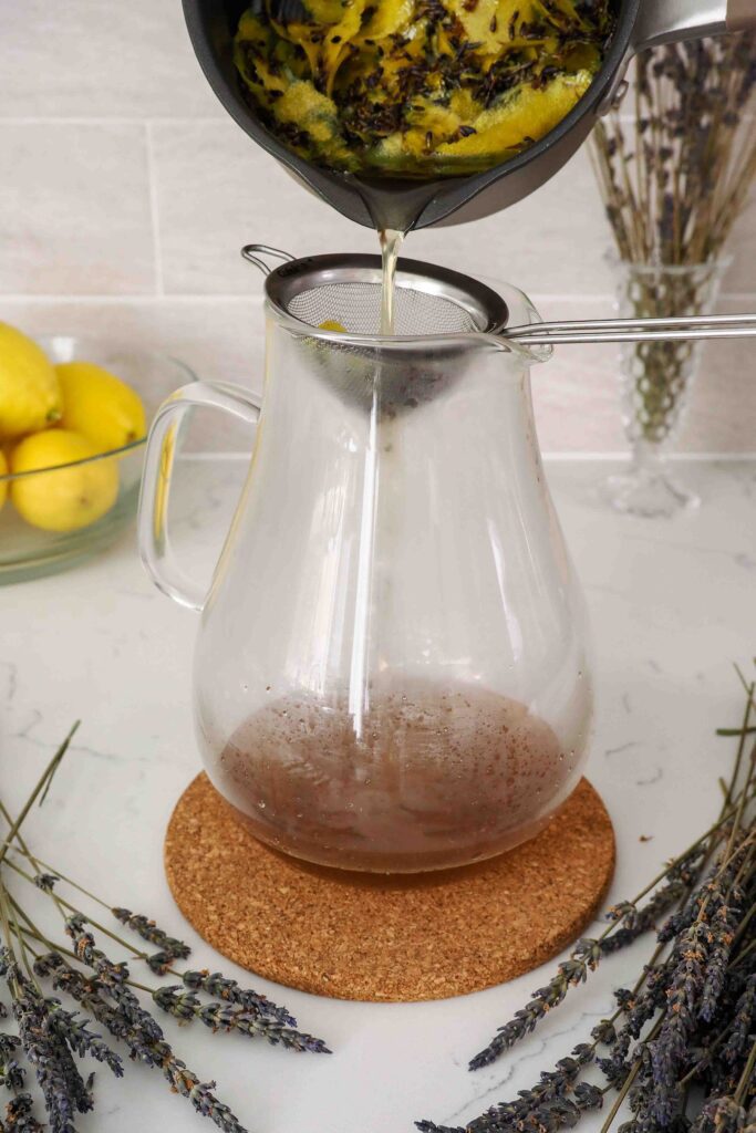 Lemon lavender simple syrup is strained from a small pot into a large pitcher.
