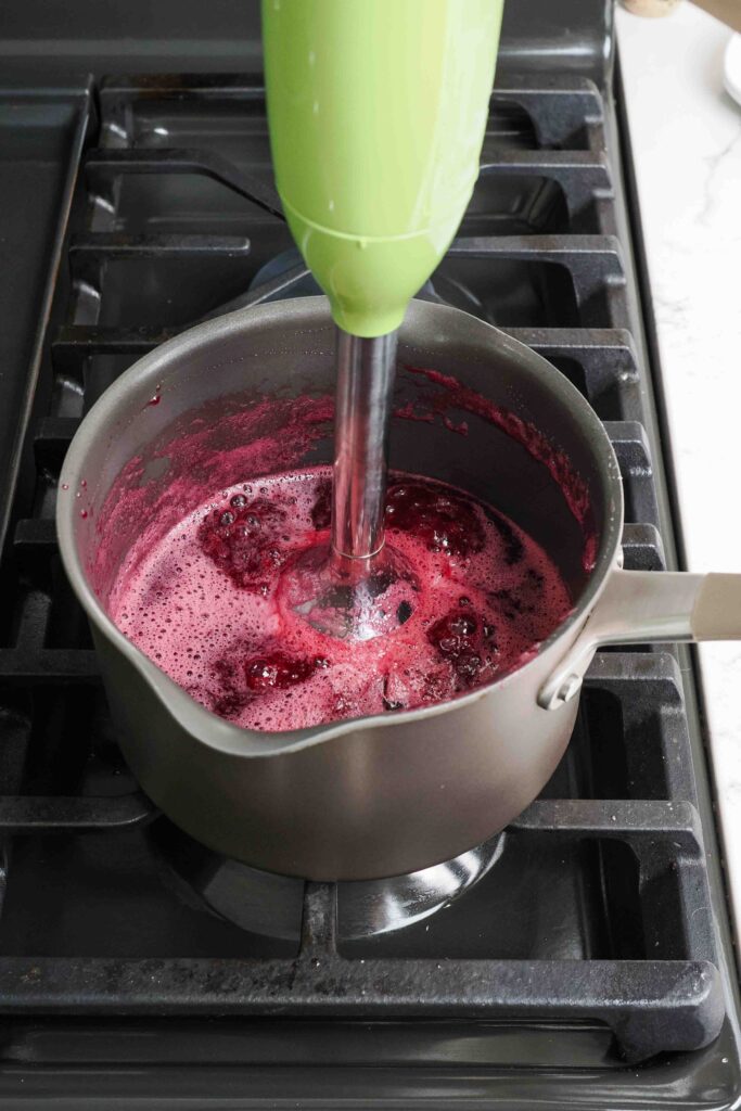 An immersion blender in a pot of cherry jam.
