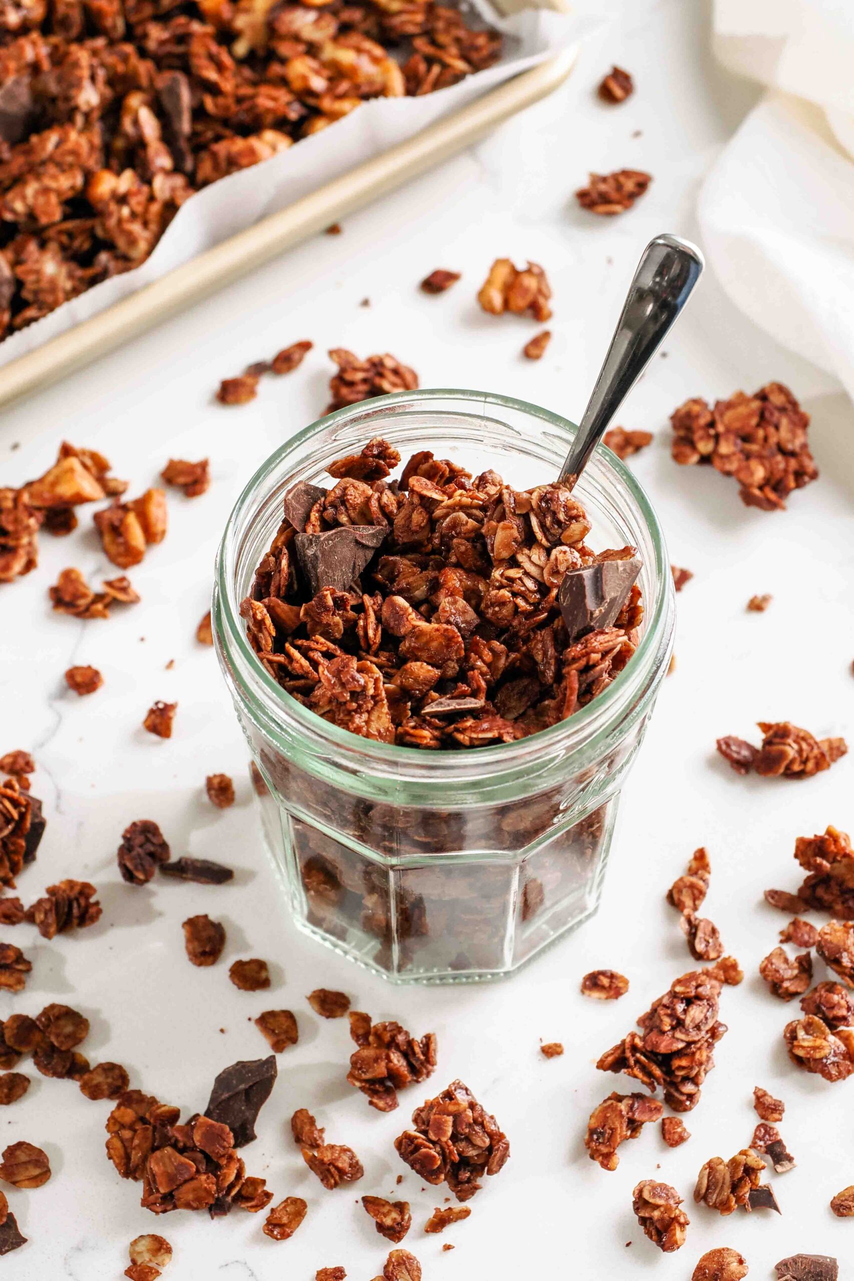 Dark chocolate granola in a glass jar with a small spoon.