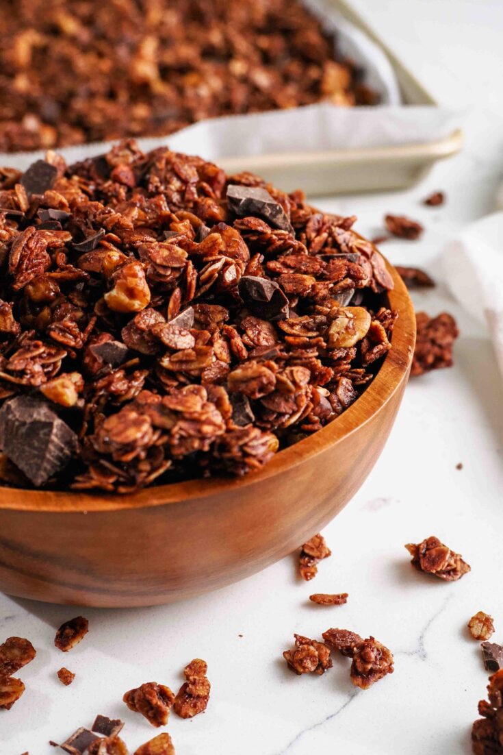 A wooden bowl is filled with dark chocolate granola and chocolate chunks.