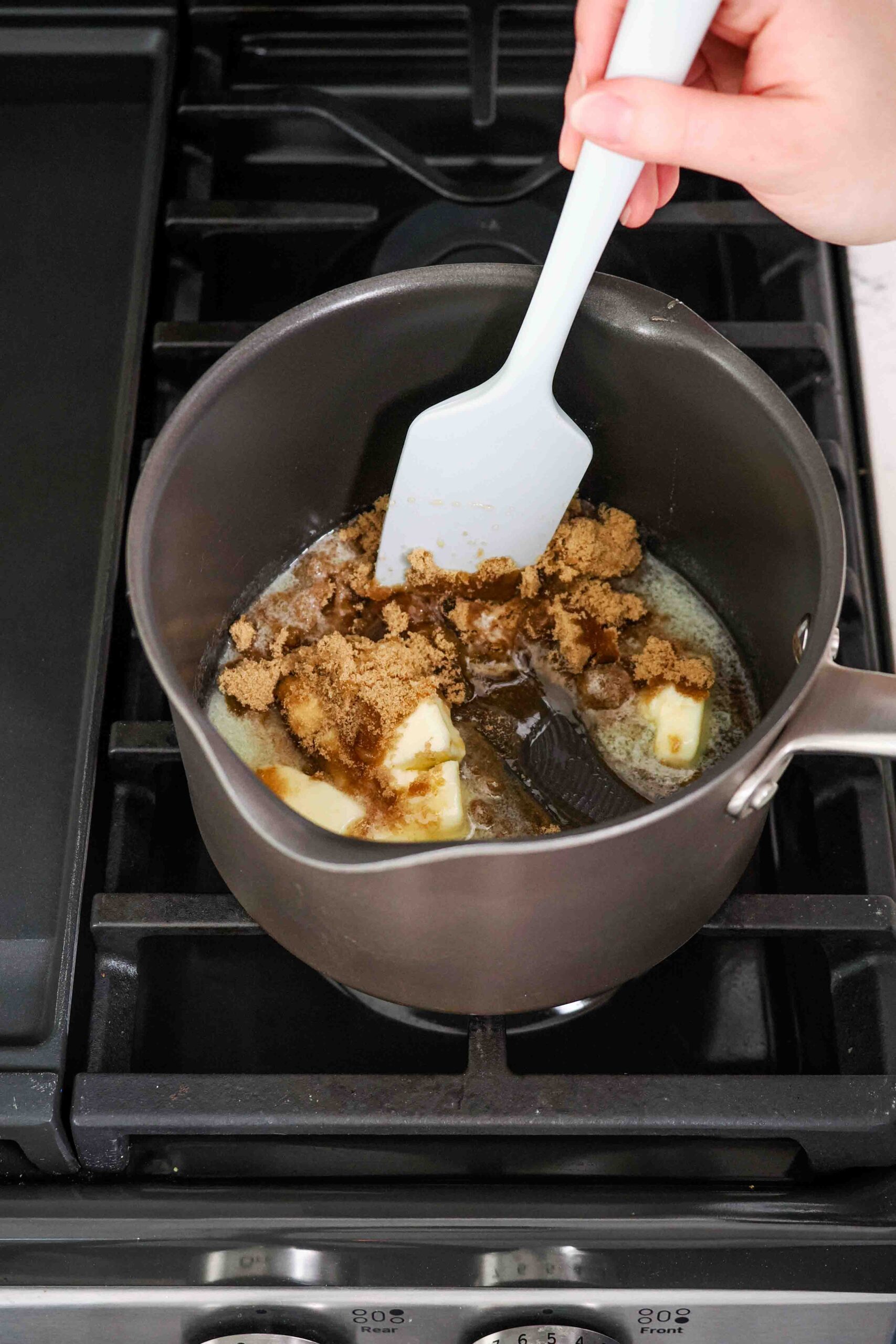 A spatula begins stirring butter, brown sugar, and honey together in a medium pot over the stove.