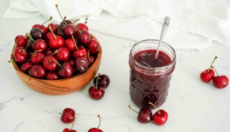 A half-pint jar of cherry jam by a bowl of cherries.