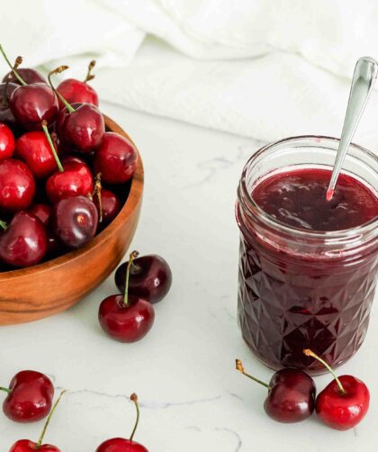A half-pint jar of cherry jam by a bowl of cherries.