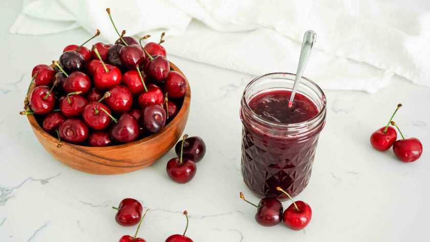 A half-pint jar of cherry jam by a bowl of cherries.