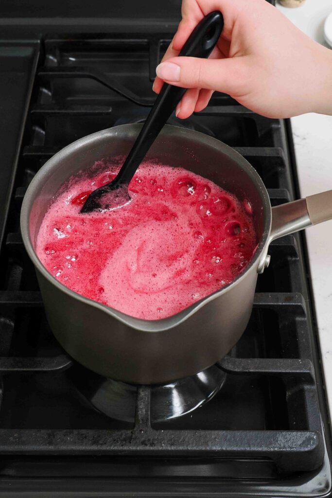 A spatula stirs cherry jam in a rolling boil.