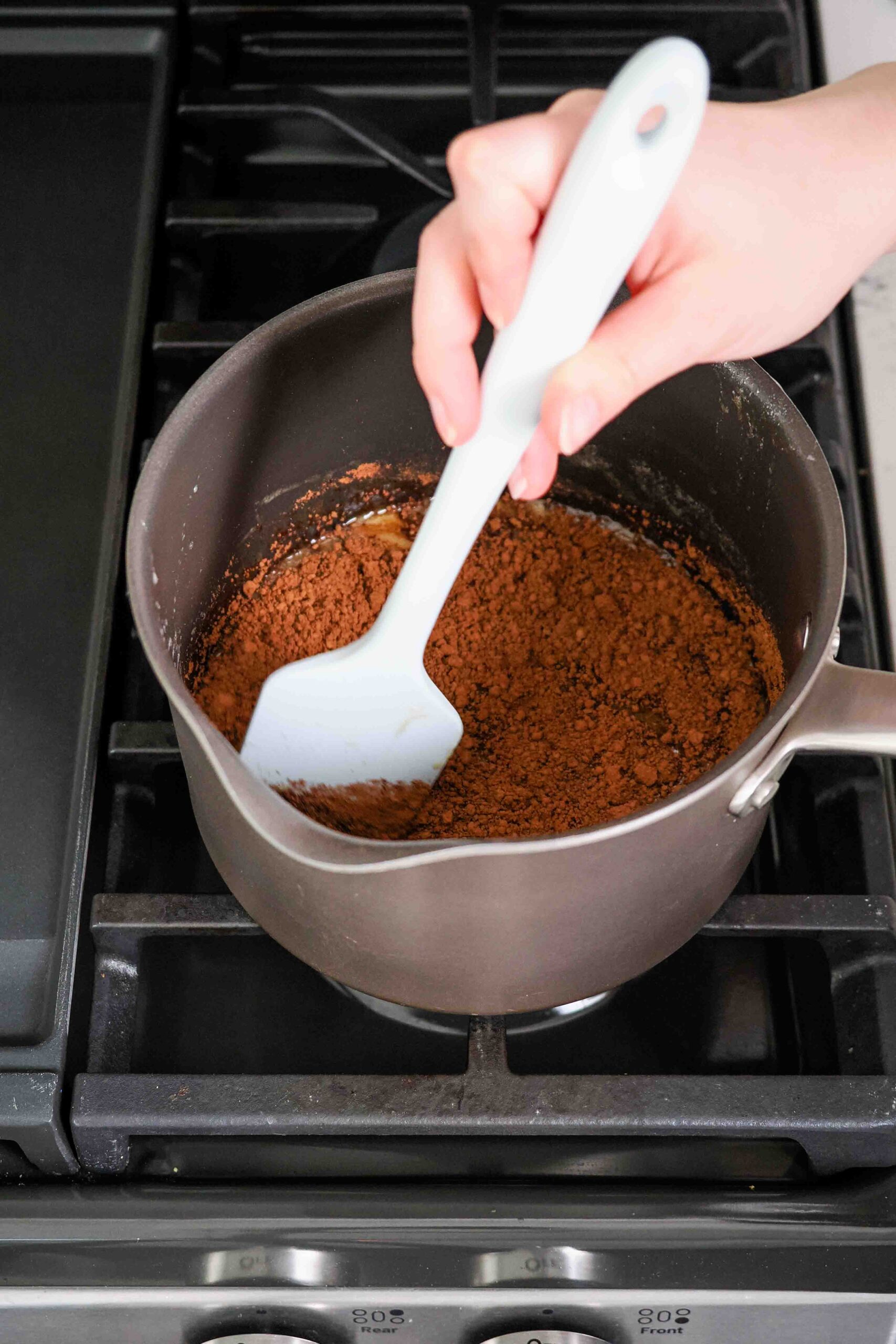 A spatula stirs cocoa powder into a granola syrup base.