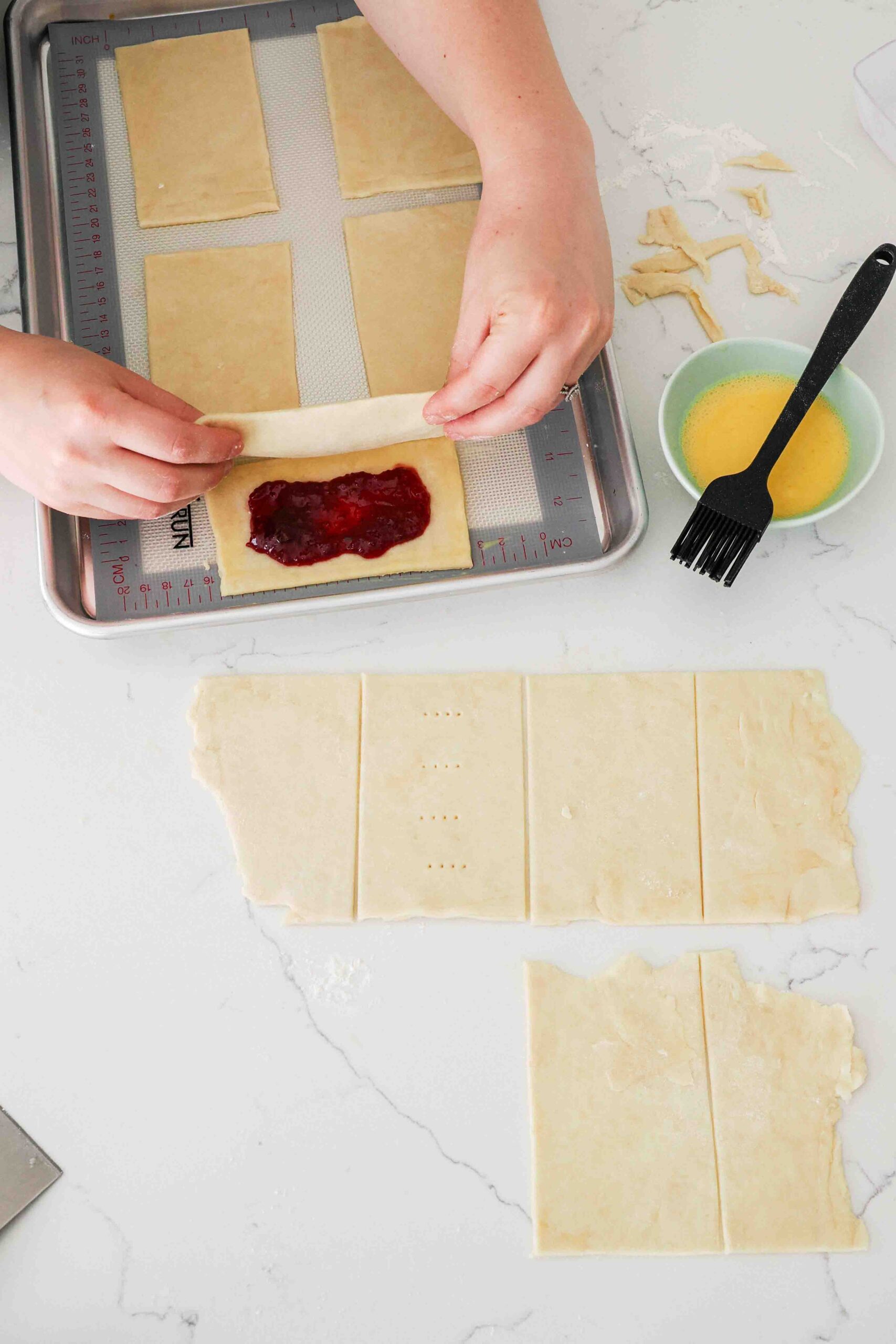 Two hands gently place a rectangle of pie dough over another topped with jam.