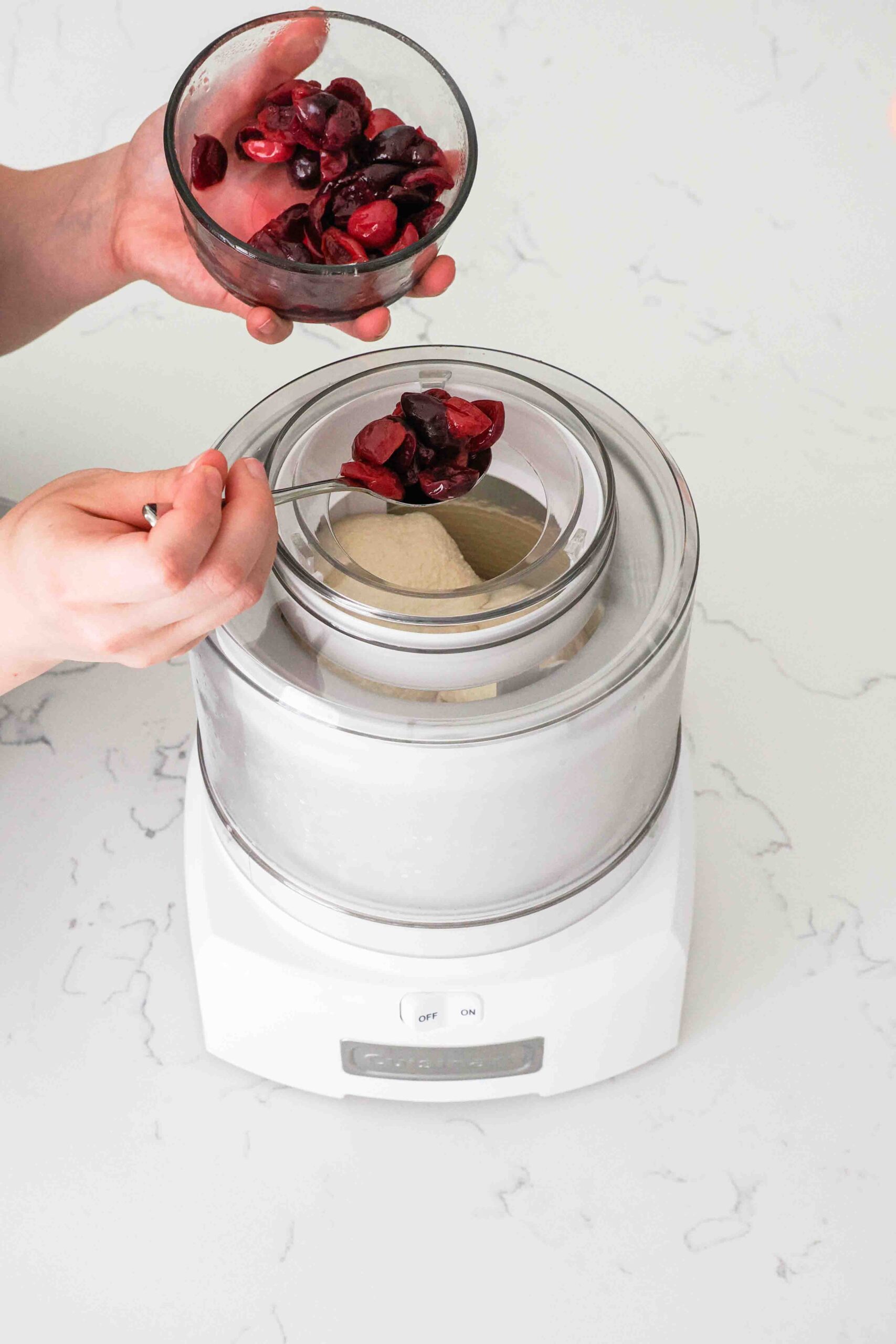 A spoonful of softened cherries are added to the churning cherry custard.