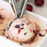 A scoop of cherry ice cream with a cherry swirl in an ice cream container.