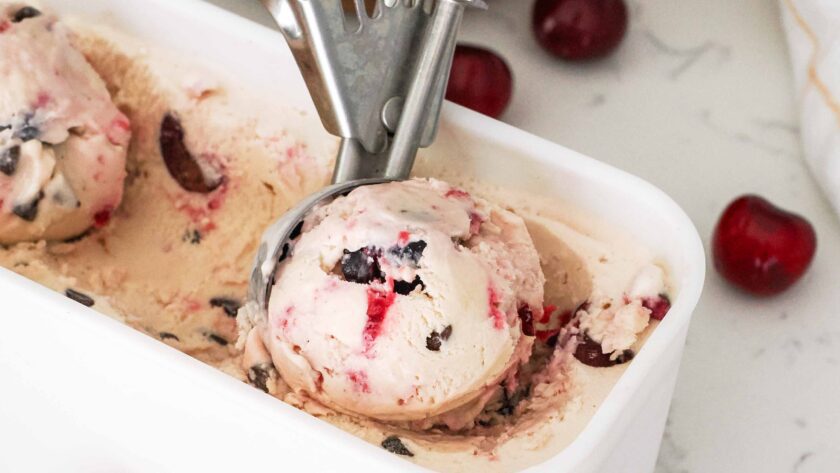 A scoop of cherry ice cream with a cherry swirl in an ice cream container.