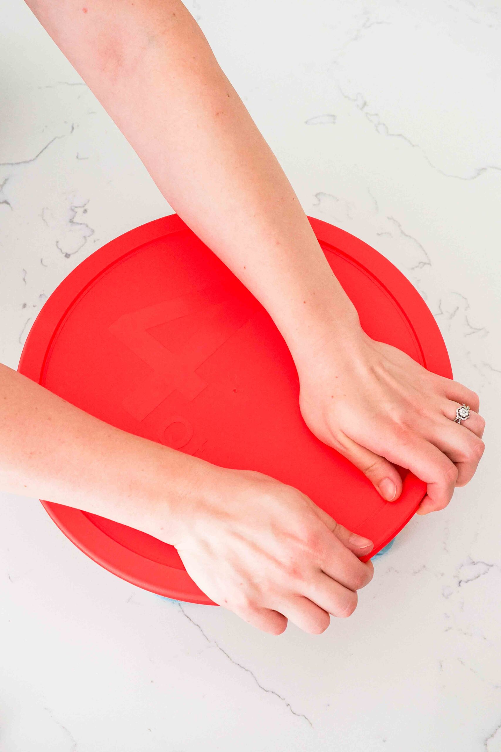 Two hands cover a glass bowl with a red lid.