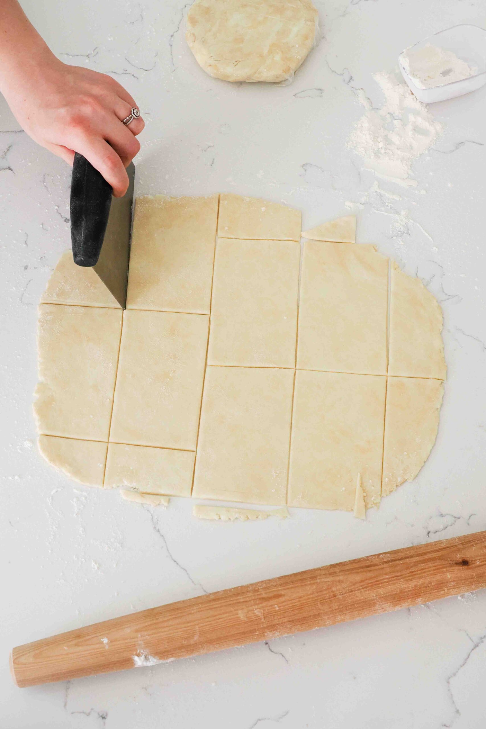A hand uses a bench scraper to cut out rectangles of pie dough.