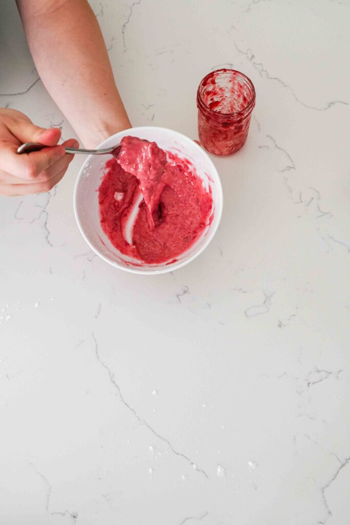 Bright pink cherry frosting drizzles off a spoon into a white bowl.
