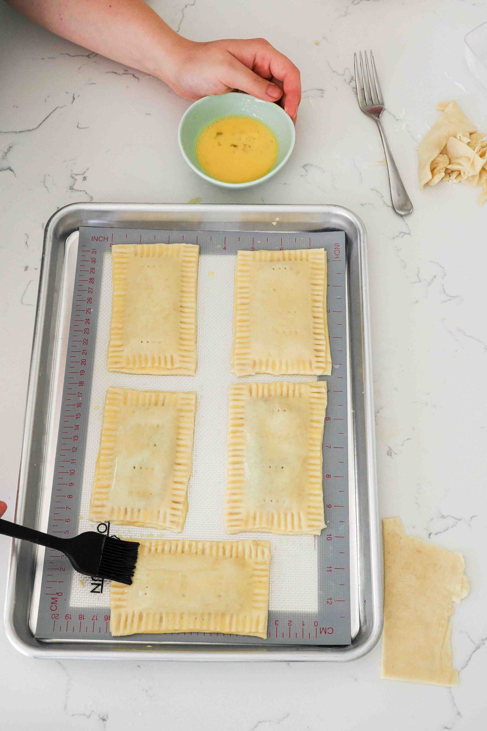 Egg wash is brushed onto homemade pop tarts with a pastry brush.