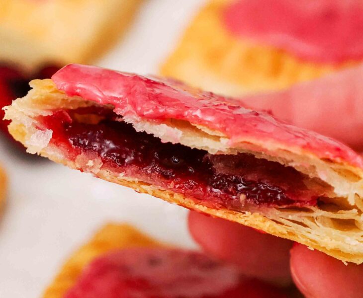A hand holds up half of a homemade cherry pop tart with the filling showing inside.