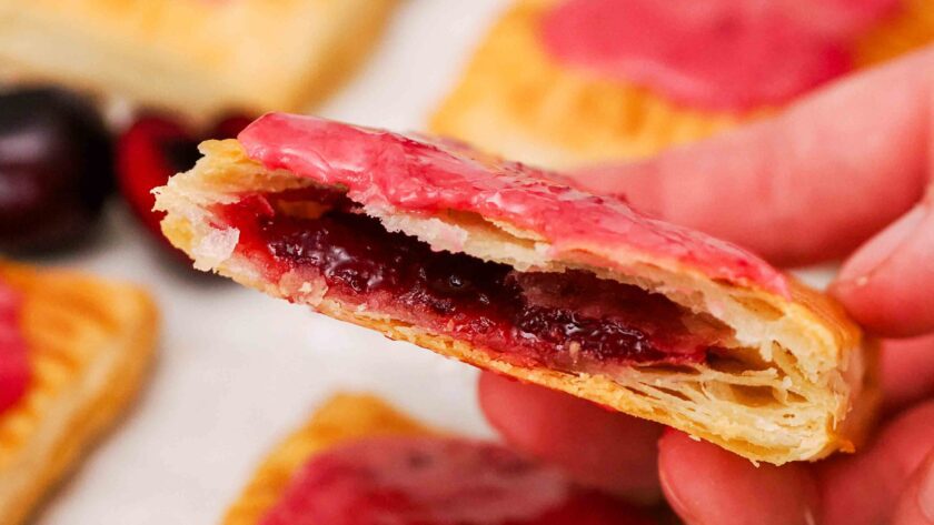 A hand holds up half of a homemade cherry pop tart with the filling showing inside.
