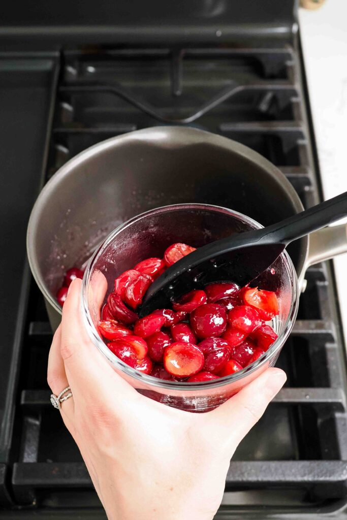 Cherries are removed from a pot with a slotted spoon into a glass container.