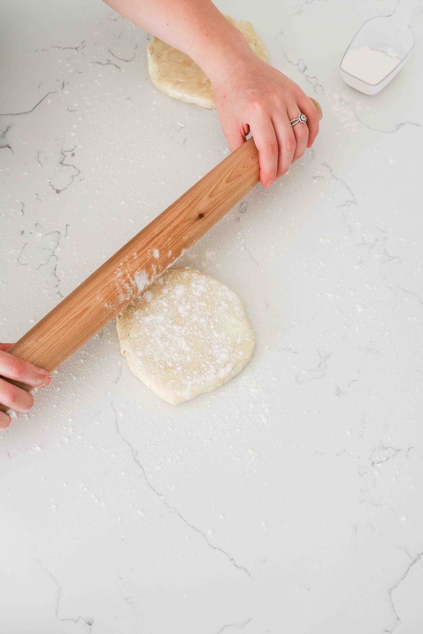 Two hands use a wooden rolling pin to flatten pie dough.