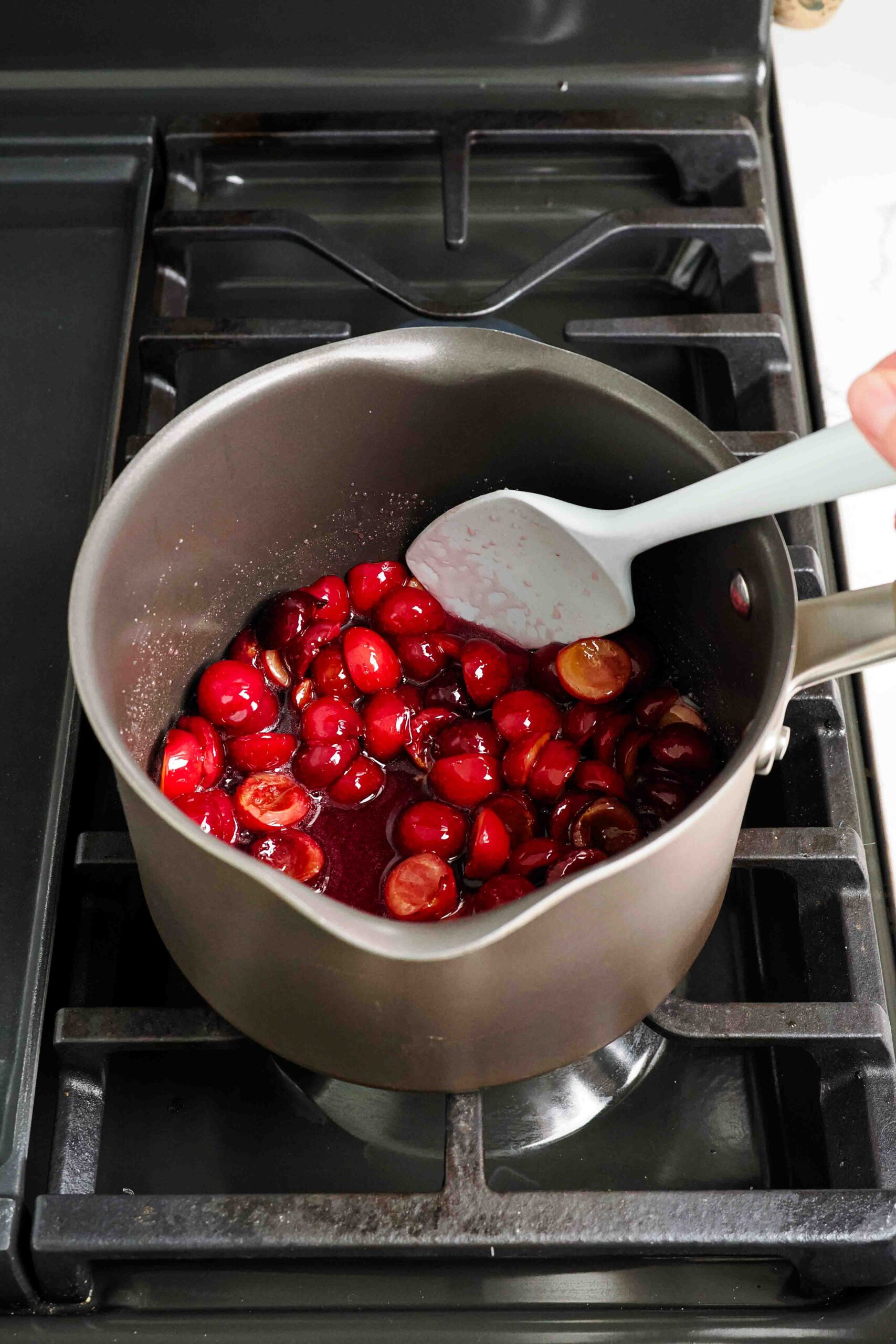 A spatula stirs cherries and sugar in a pot over the stove.