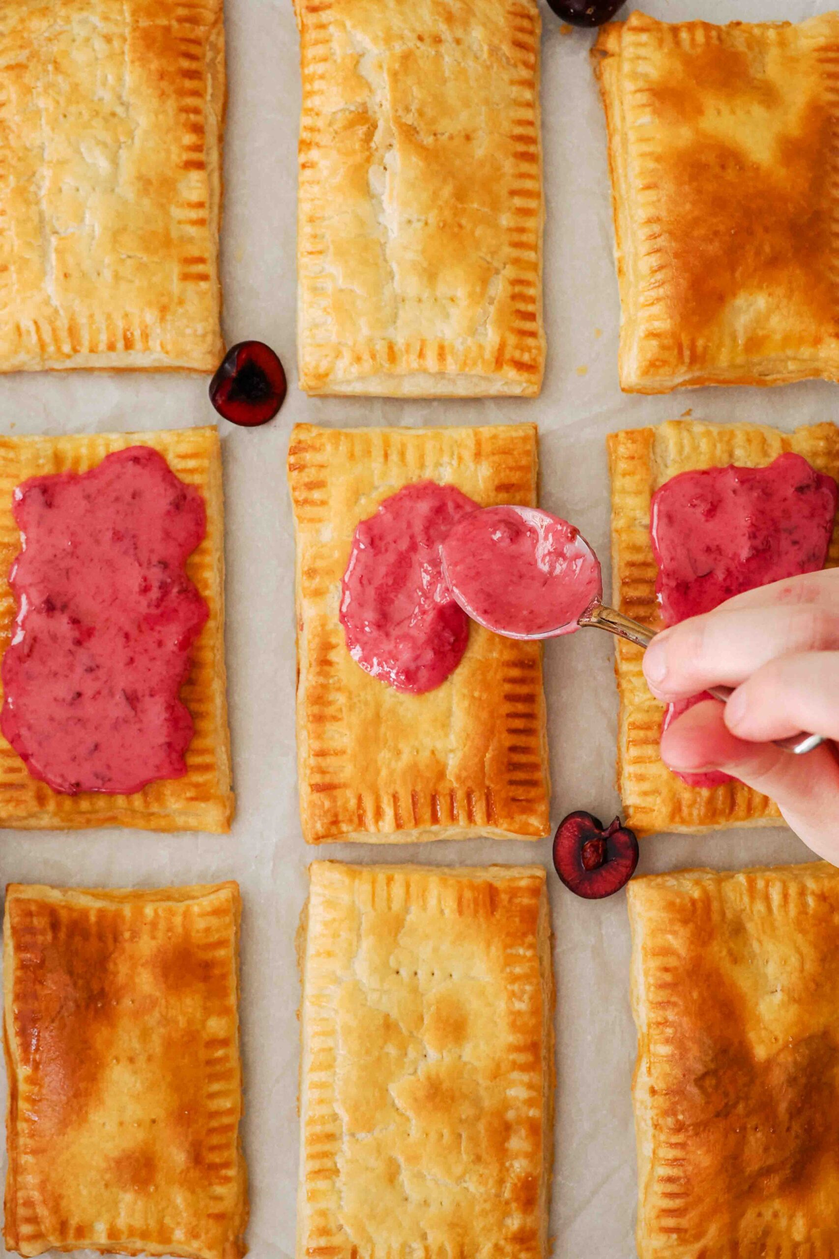 A spoon spreads cherry frosting on homemade cherry pop tarts.