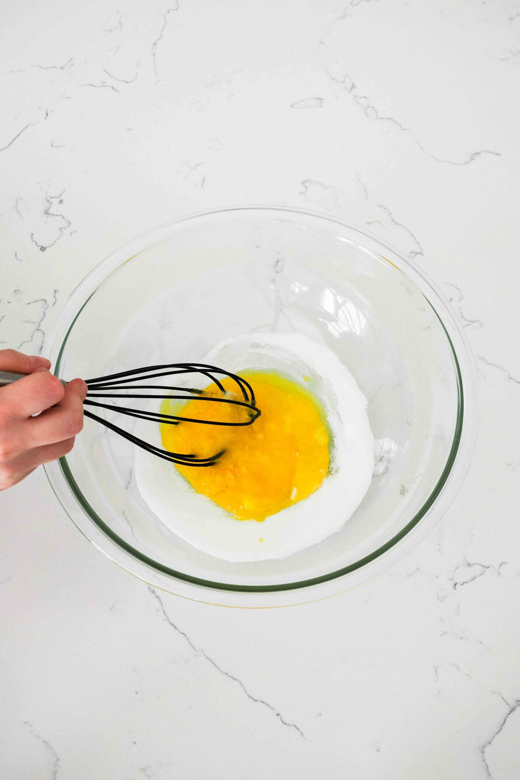 Egg yolks and sugar in a glass bowl beginning to be whisked together.
