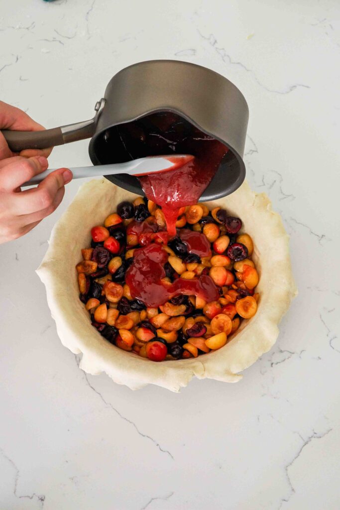 The thickened cherry filling is poured over the cherries in the pie pan.