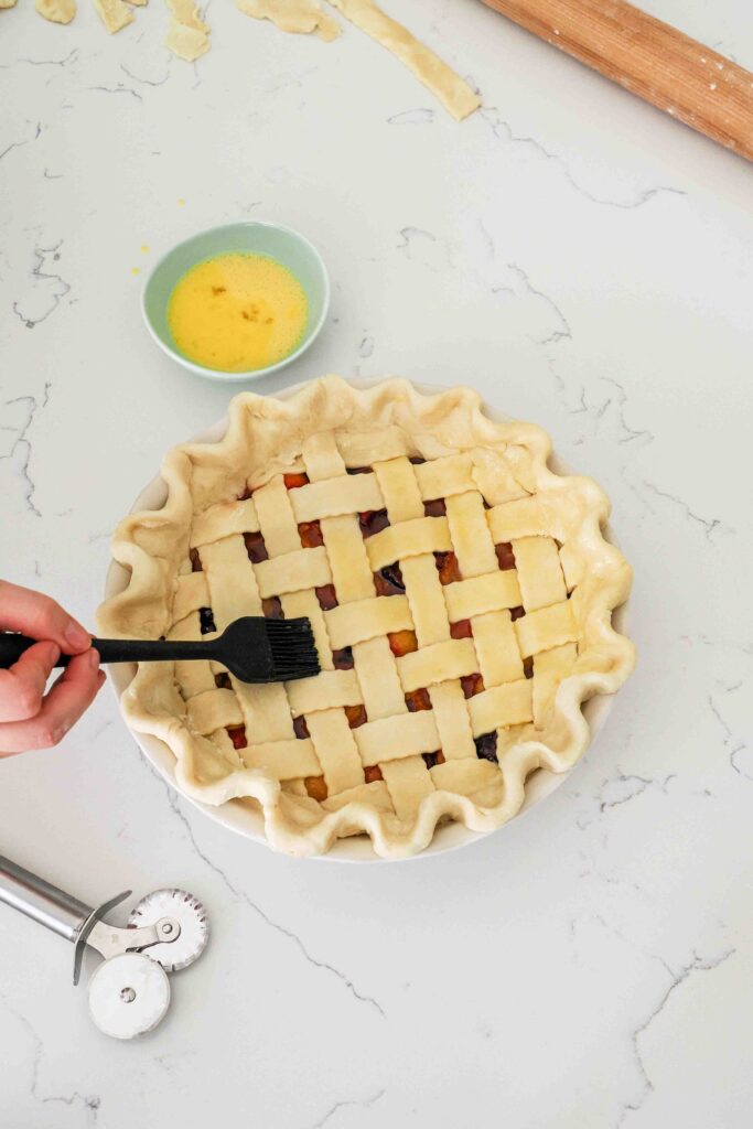 Egg wash is brushed onto an unbaked cherry pie.