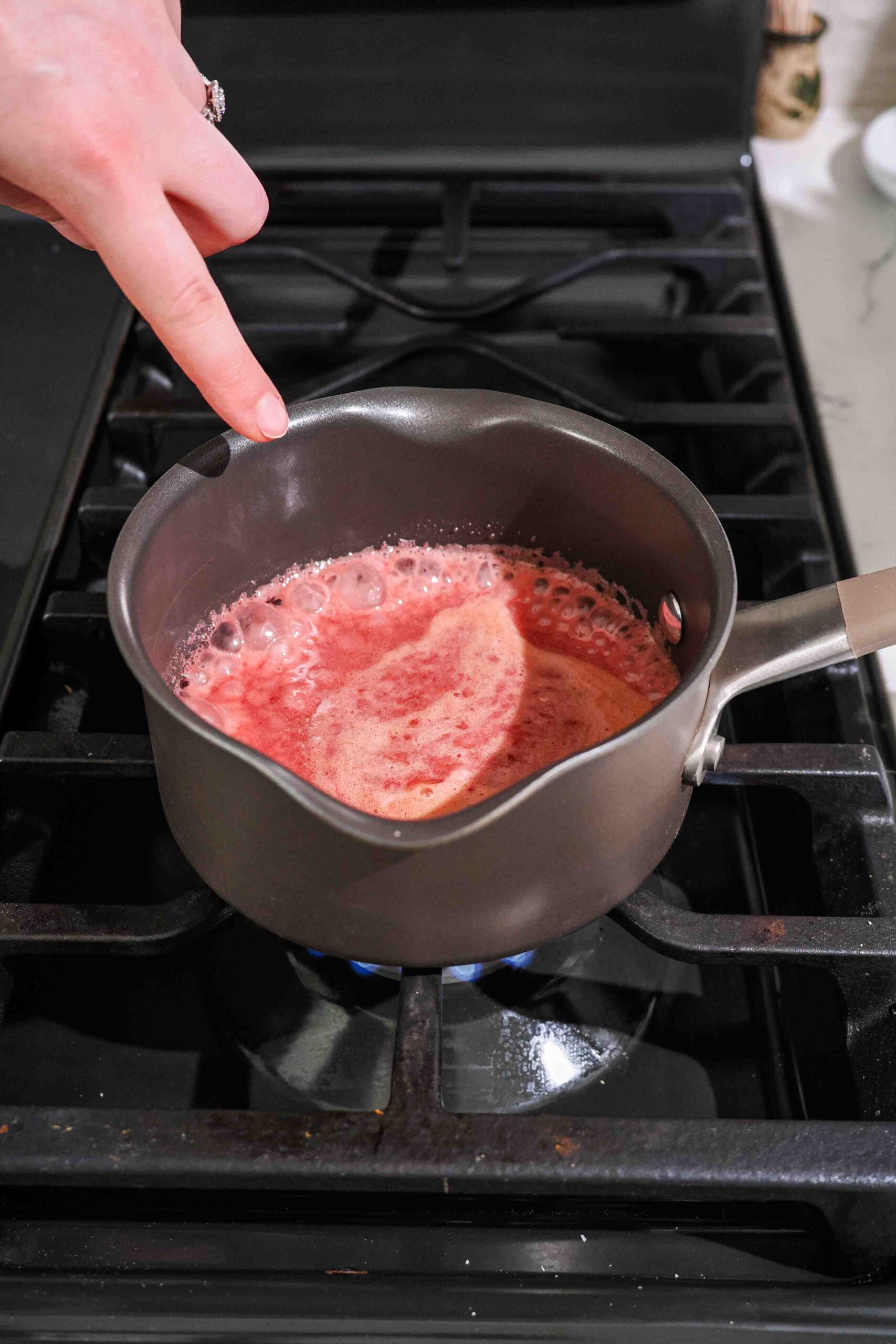 Red cherry liquid boils in a small saucepan over the stove.