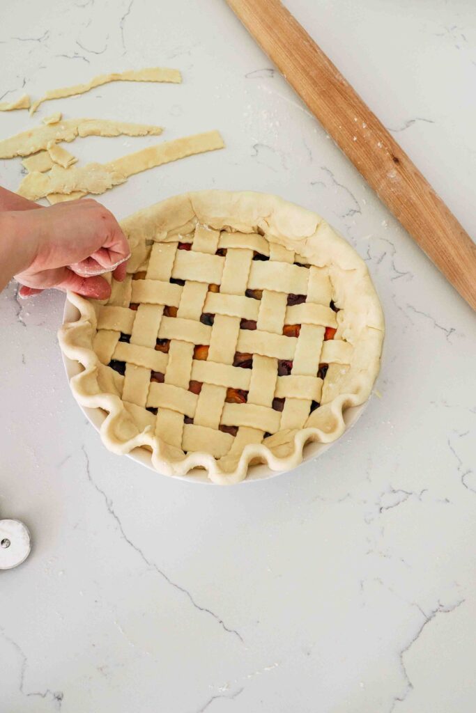 Two hands crimp together the edges of pie dough to make a decorative ruffle.