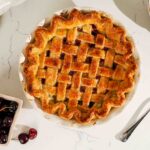An overhead image of a golden brown cherry lattice pie with almond extract.