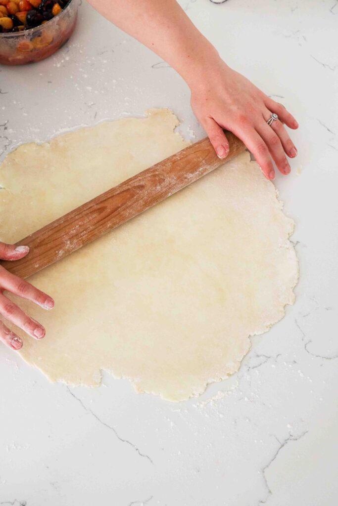 Two hands roll out a sheet of pie dough.