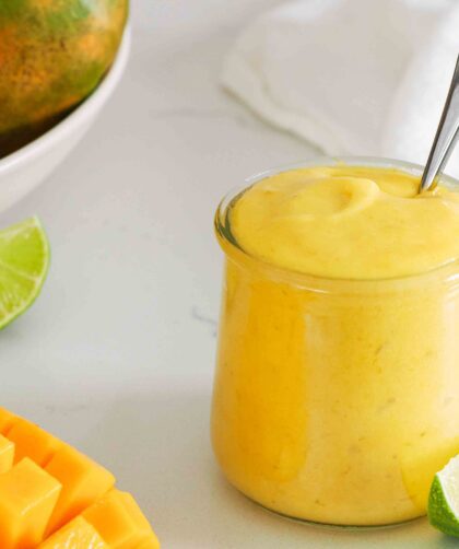 A small jar of mango curd with a lime wedge and slice of mango nearby.