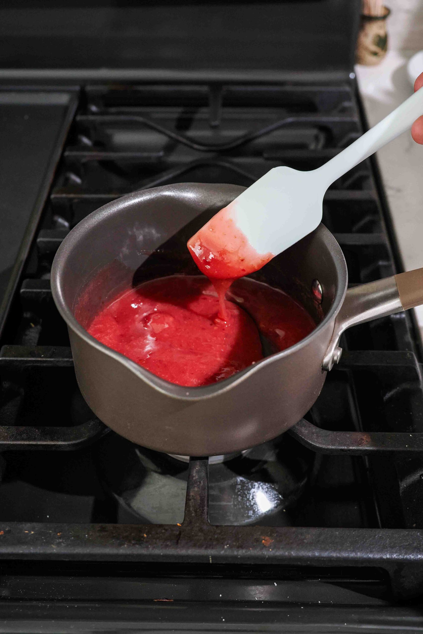 A spatula drips thickened cherry filling back into a saucepan on the stove.
