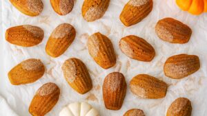 An overhead image of pumpkin madeleines partially dipped in cinnamon sugar on crumpled parchment paper.