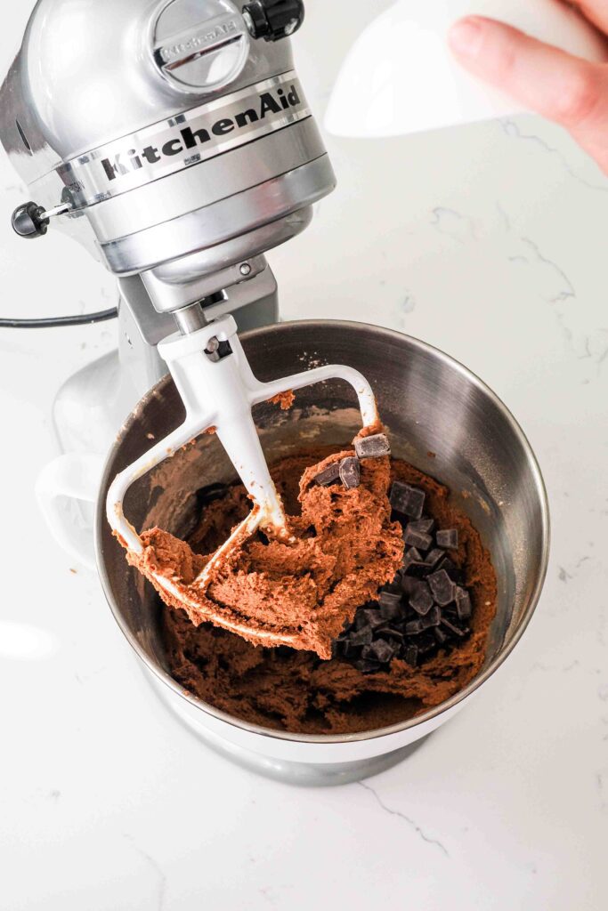 Chocolate chips are poured into a mixing bowl with chocolate cookie dough.