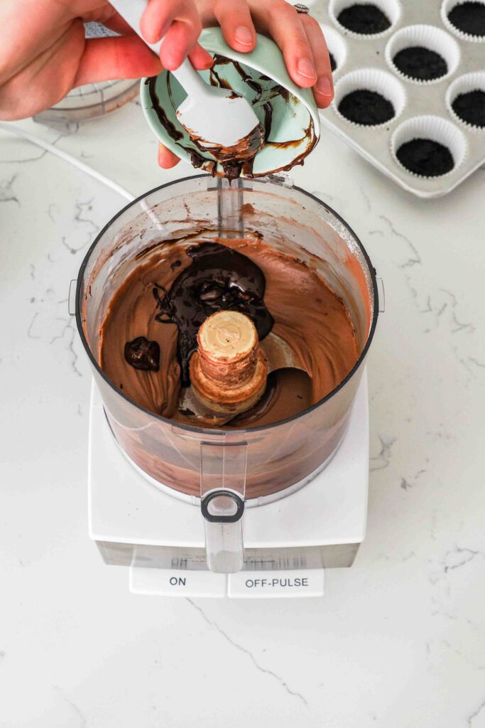 Melted chocolate is poured into the bowl of a food processor with chocolate cheesecake filling.